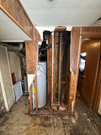 A gutted interior wall with exposed plumbing and an old water heater — a home Hidden Gems bought as-is